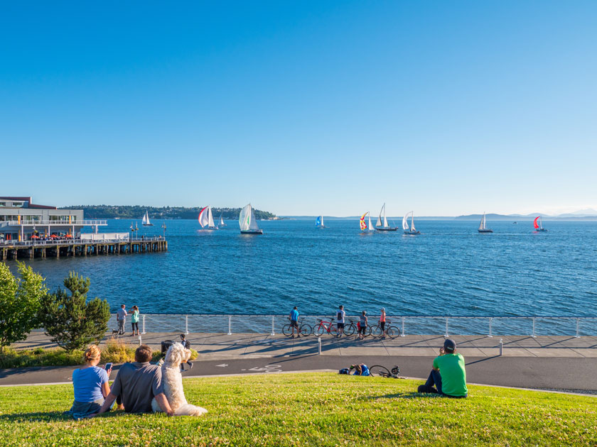 Elliot Bay Trail with kids in Seattle, offering scenic views of the Seattle waterfront and piers. This photo is taken from the grassy hills of Olympic Sculpture Park, where families can enjoy a relaxing walk or bike ride with sweeping views of Elliott Bay, boats, and the city skyline in the distance.