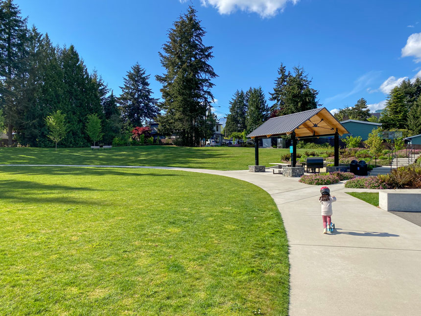 Young girl riding her scooter around the paved loop at Surrey Downs Park in Bellevue, a popular family-friendly park with wide paths, open green space, and a modern playground.