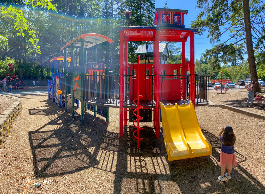 Wilburton Hill Park playground in Bellevue, featuring a colorful train-themed play structure with multiple slides, climbing features, and imaginative play areas for young children.