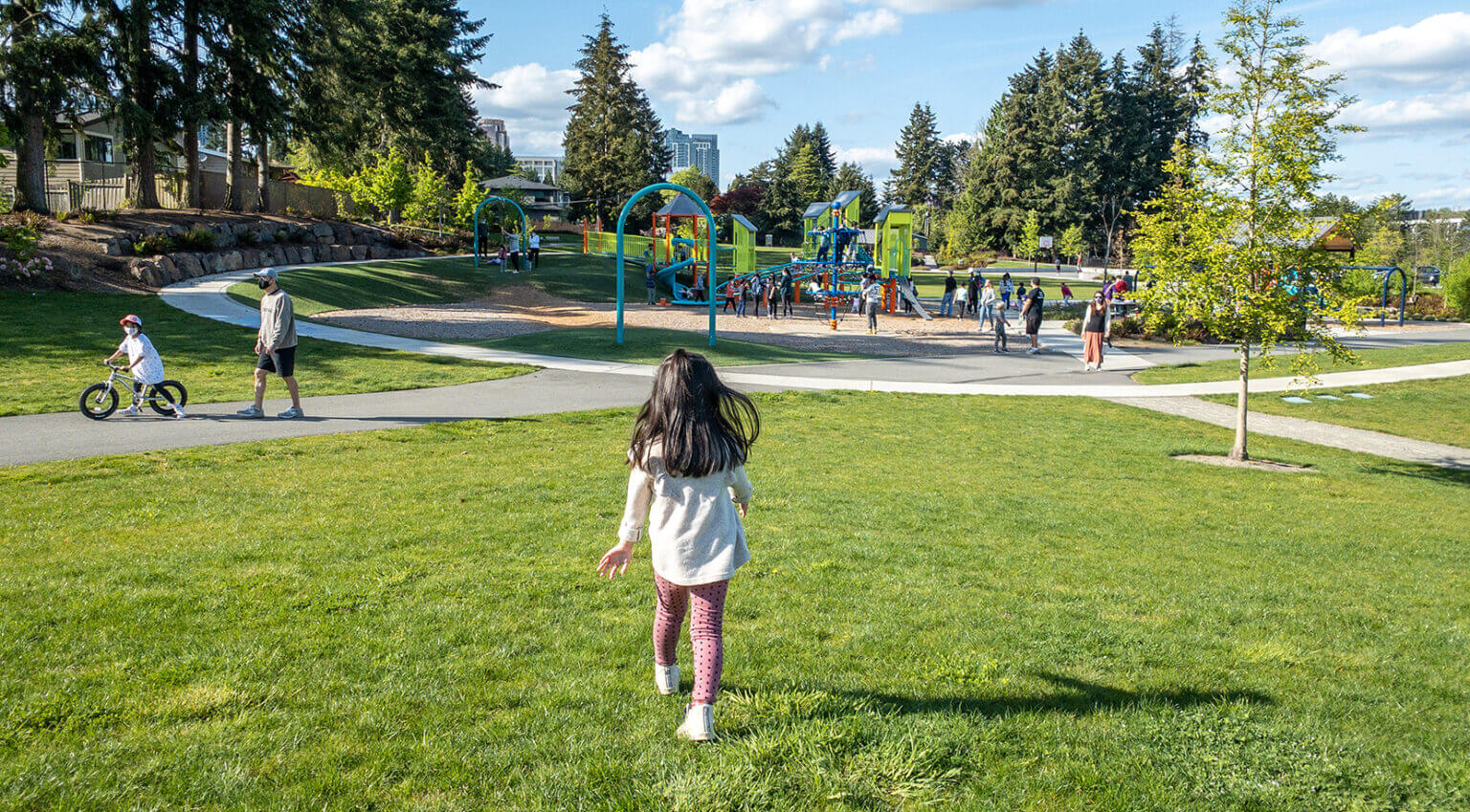 Toddler girl running across the open grassy fields toward the playground at Surrey Downs Park in Bellevue, Washington. This family-friendly park features wide open spaces, shaded picnic areas, and a well-designed playground with structures for both toddlers and older kids—making it a great destination for outdoor play and gatherings on the Eastside.