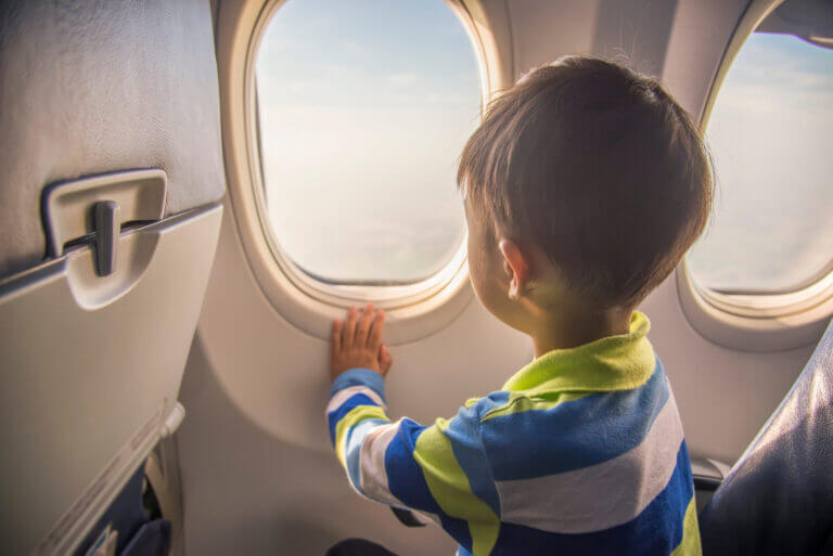 Boy looking out of the airplane window while flying in the sky, a moment from a family trip. Flying with kids tips
