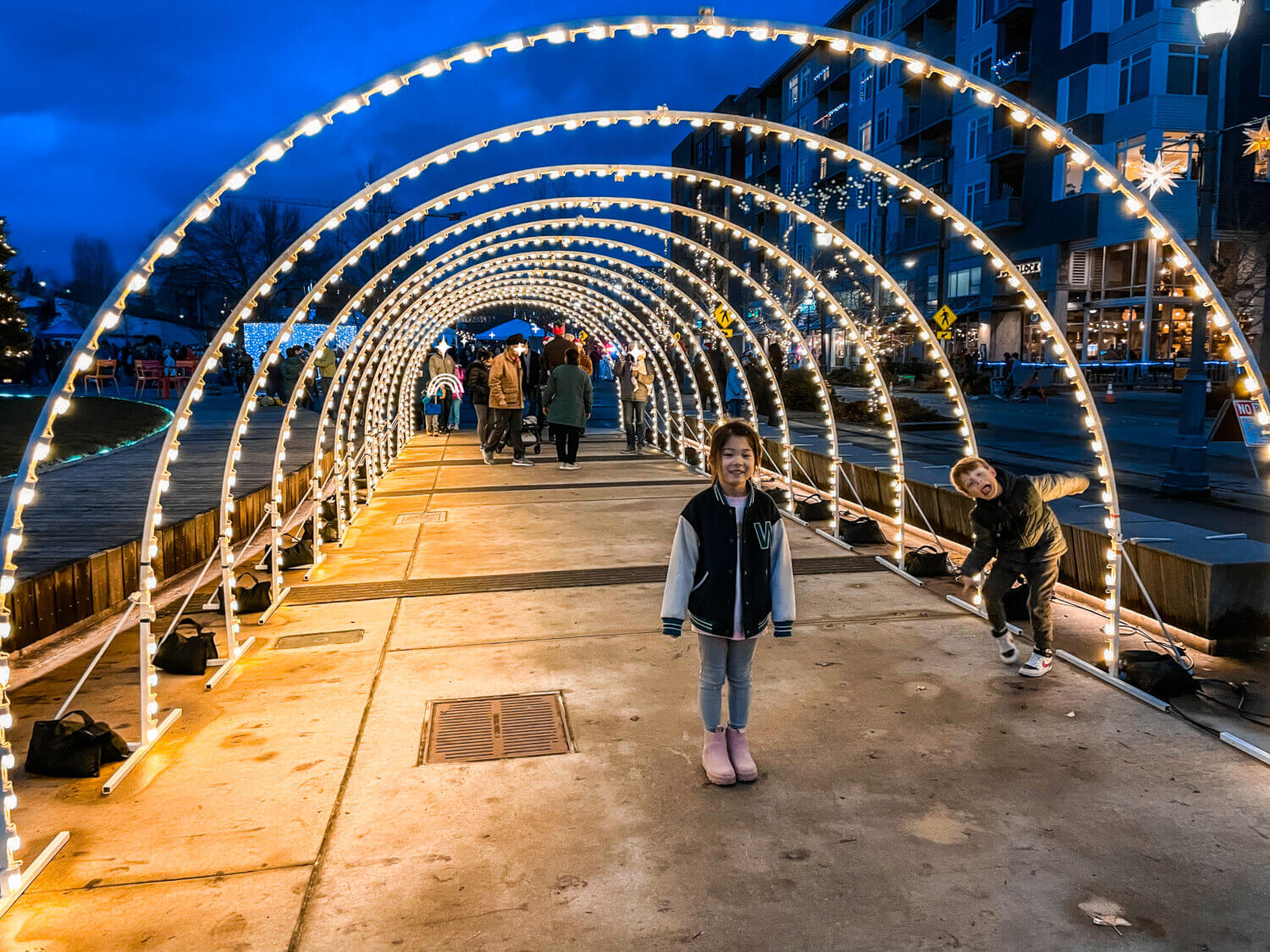 Redmond Downtown Holiday Lights create a magical winter wonderland, with kids joyfully taking photos under the beautifully lit festive tunnel. This dazzling light display transforms the area into a family-friendly holiday destination, perfect for capturing special moments and making cherished memories during the festive season.