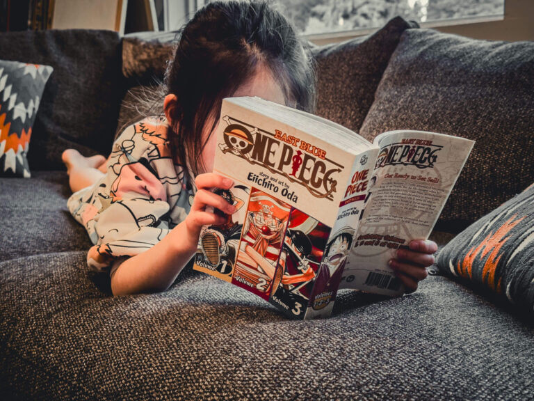 Young girl on a couch reading One Piece Manga, a popular Japanese story great for kids. Here is a book review for parents.
