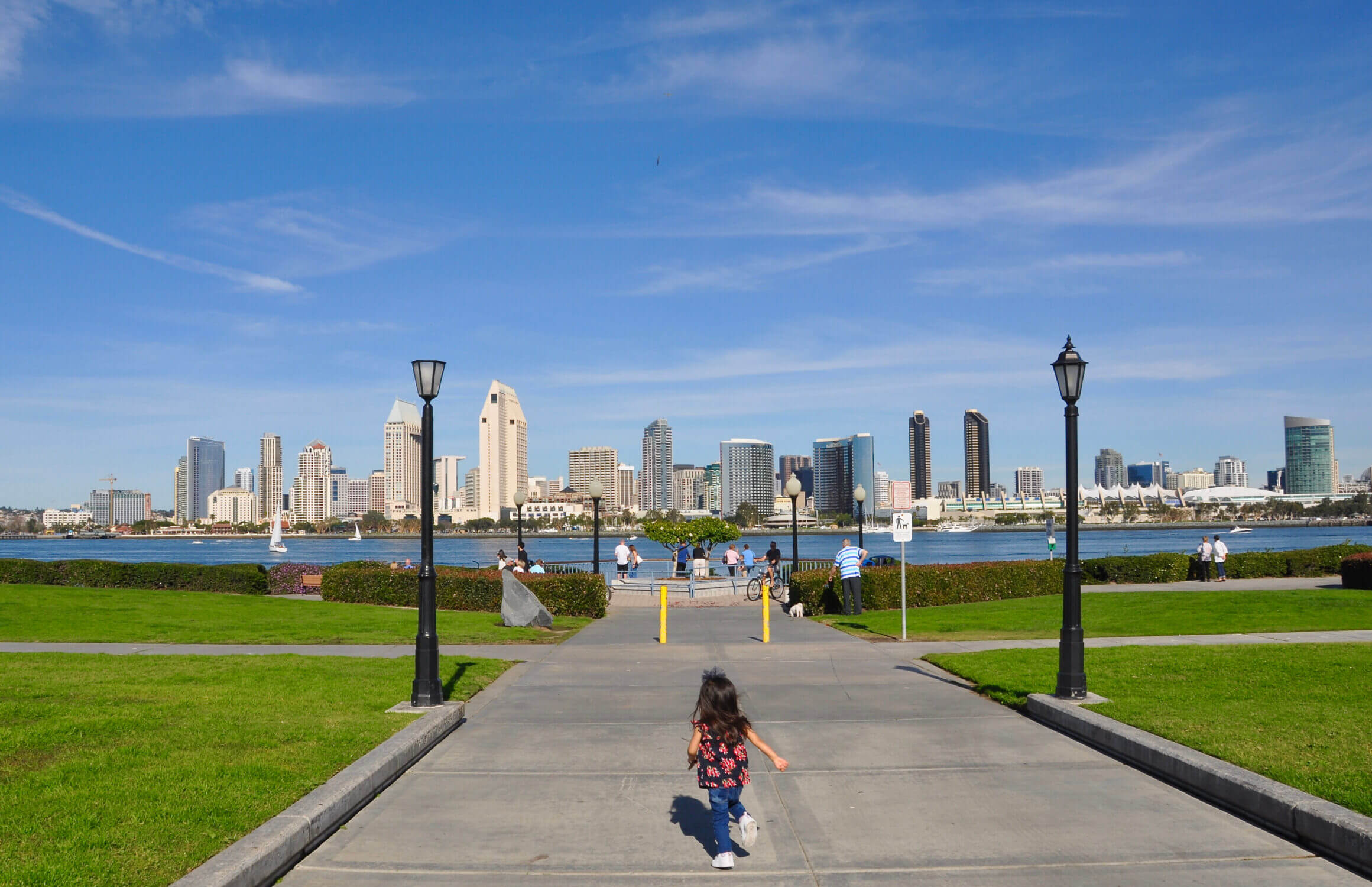 Centennial Park, a scenic waterfront gem in Coronado, offers stunning panoramic views of downtown San Diego. A little girl excitedly runs toward the waterfront, taking in the breathtaking skyline across the bay. This peaceful park is a favorite family-friendly spot, featuring open green spaces, benches, and walking paths perfect for a leisurely stroll.