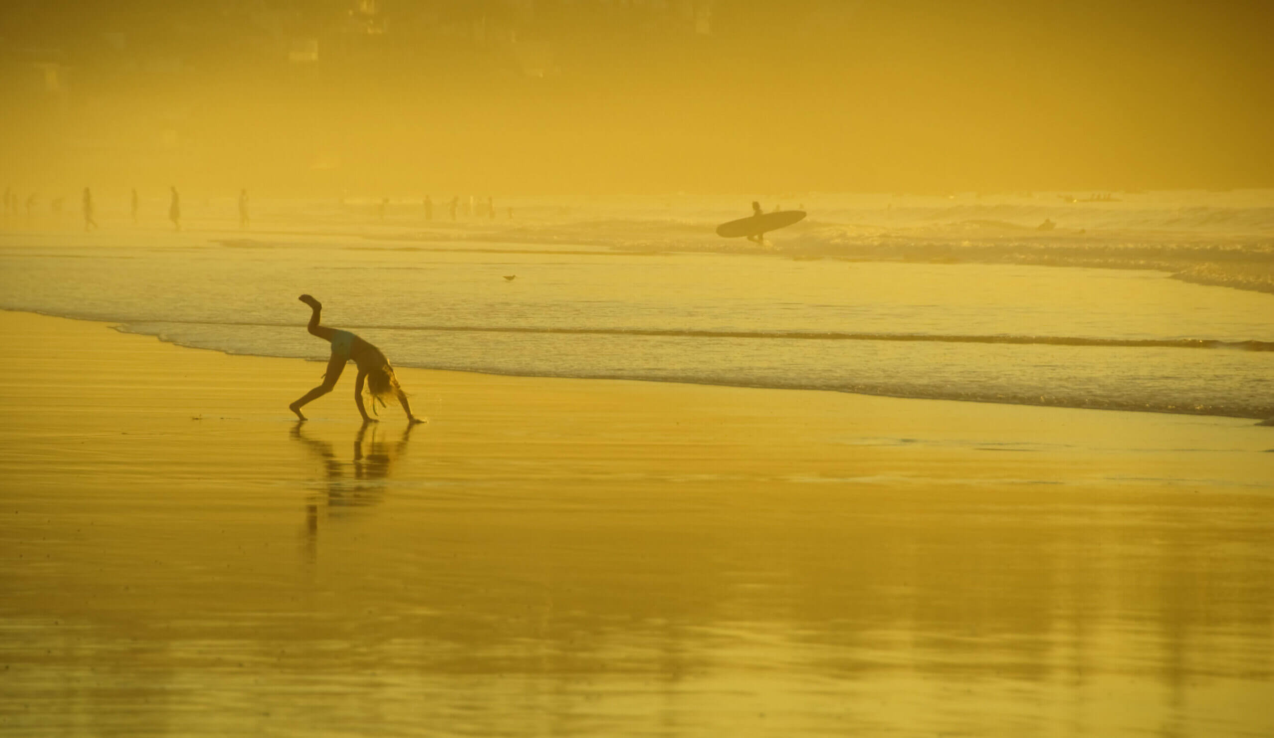 Kid playing on the beach at sunset, doing a somersault on the sand near the water at La Jolla Shores in San Diego, California. A popular family vacation destination.