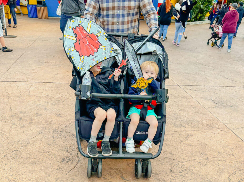Dad pushes his two young sons in a double stroller through LEGOLAND California, making it easier to navigate the park with toddlers. LEGOLAND is stroller-friendly with wide paths, shaded rest areas, and plenty of kid-focused attractions, making it an ideal theme park for families with little ones