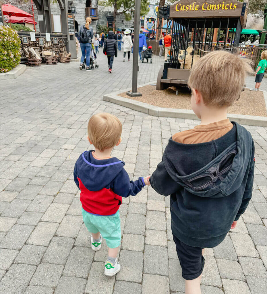 Older brother holding his toddler brother’s hand as they walk into LEGOLAND California, capturing a heartwarming family moment. This image is part of a two-day itinerary and guide for visiting LEGOLAND with kids, filled with tips and must-see attractions for families.