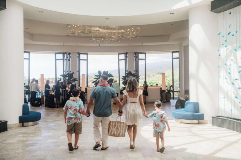 Mom, dad, and two young boys walking hand in hand through the open-air lobby at the Outrigger Kona Resort on the Big Island of Hawaii. This welcoming and spacious resort is ideal for families, offering cultural programs, oceanfront views, and a kid-friendly pool with a waterslide—making it a perfect home base for an unforgettable Hawaii family vacation