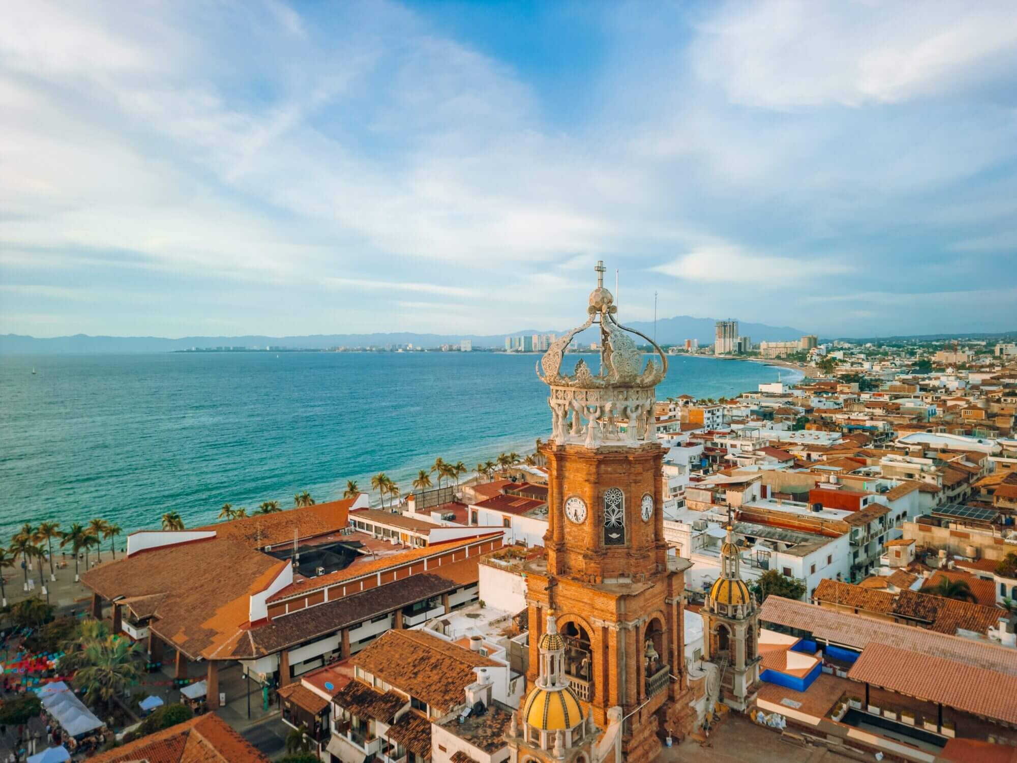 Aerial view of Puerto Vallarta, Mexico, showcasing the colorful cityscape with the iconic Lady of Guadalupe Church in the foreground and the sparkling Pacific Ocean in the background. This picturesque town is a top family vacation destination known for its beaches, culture, and kid-friendly activities.