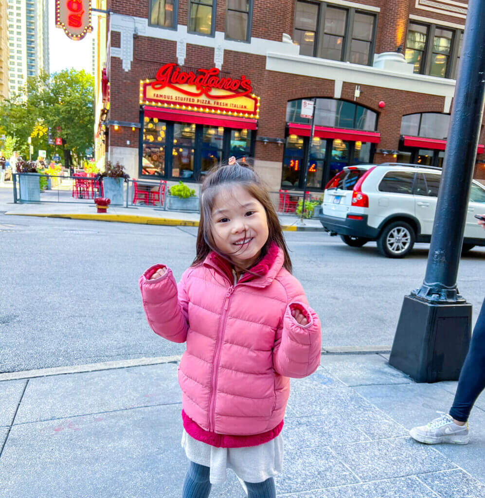 Toddler girl smiling and taking a photo in front of Giordano’s, one of the most iconic spots for deep dish pizza in Chicago—must-visit for families exploring the city with kids.
