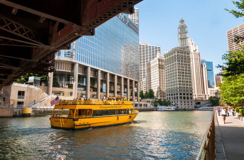 Yellow water taxi cruising along the Chicago River with iconic downtown buildings in the background—a fun and scenic way to explore the city, featured in our blog about things to do with kids in Chicago.