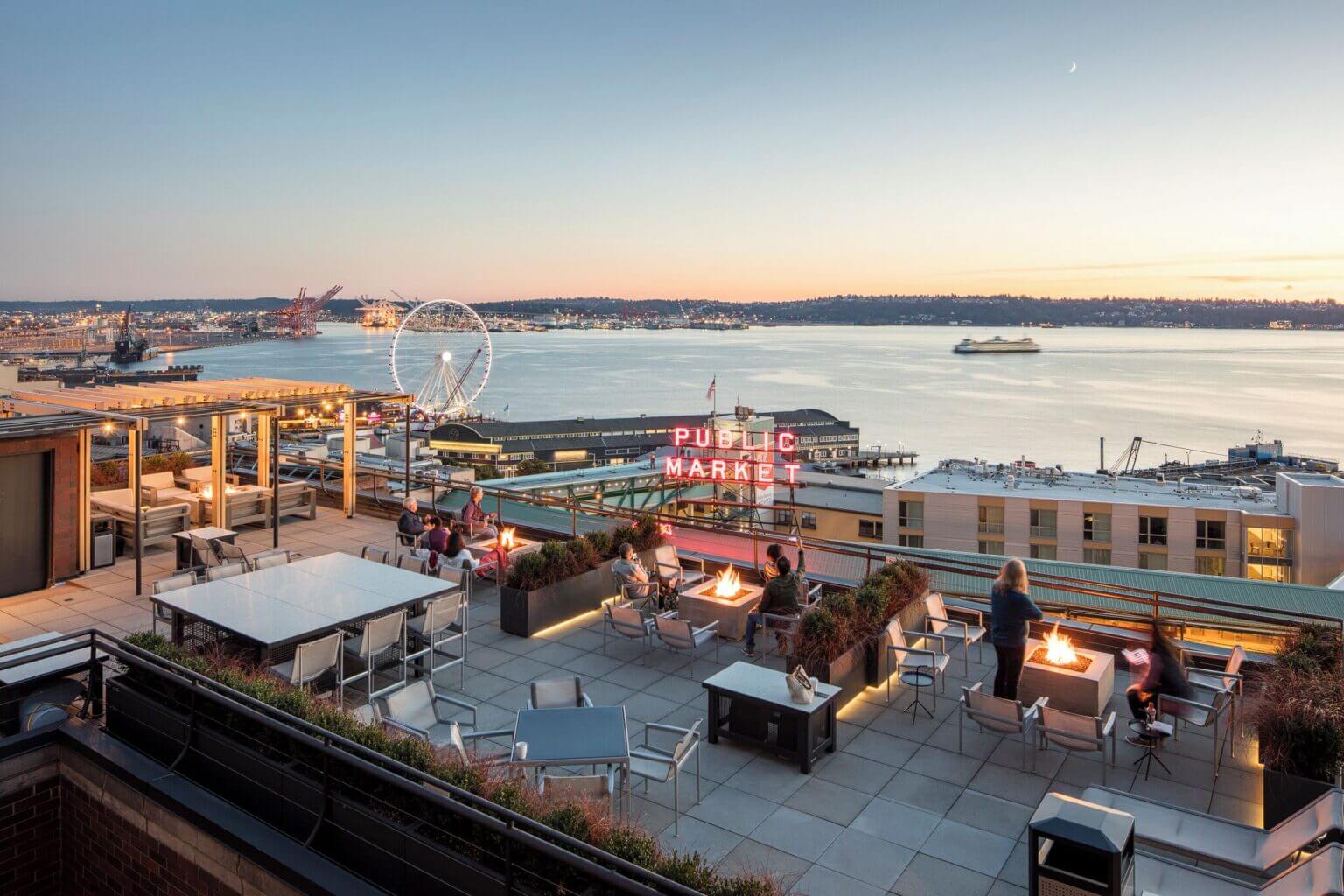 Rooftop balcony view from Inn at the Market, overlooking the iconic Pike Place Market neon sign, Seattle’s waterfront, and the Ferris wheel in the distance. A relaxing and scenic spot, perfect for families staying in downtown Seattle.
