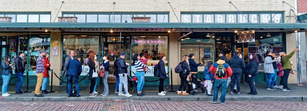 Visiting the original Starbucks at Pike Place Market in Seattle, one of the top things to do with kids. In the photo, a line of people waits outside the historic coffee shop, which still features its original brown logo and old-time storefront charm. A fun stop for coffee lovers and families alike while exploring the market.