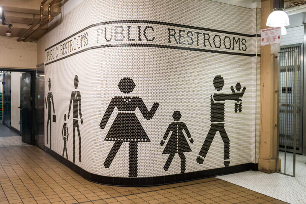 Playful and quirky wall tile art at Pike Place Market bathroom entrance showing a stick figure dad carrying a baby toward the restroom sign—funny and unexpected art that makes kids and adults alike laugh during a family outing in Seattle.